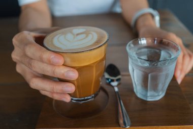 Elinde kahve fincanı ve bir bardak su tutan kişi..