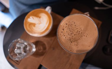 Beyaz bardakta, ahşap masada, sütlü kahvenin en iyi manzarası.