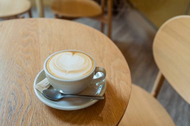 Kahve fincanı ve ahşap masada köpüklü latte..