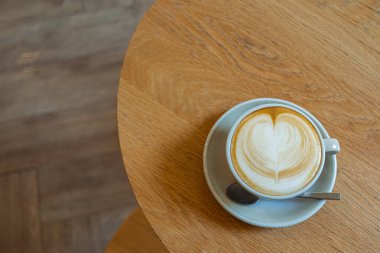 Beyaz bardakta, ahşap masada, sütlü kahvenin en iyi manzarası.