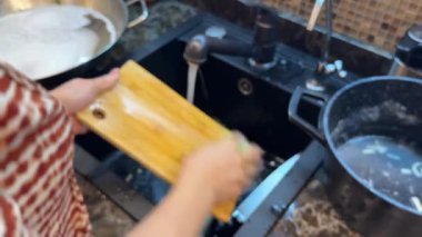 Mutfak işi sırasında lavaboda tahta kesme tahtasını sabun ve suyla yıkamak. Tanınmayan bir kadın lavaboda tahta kesme tahtasını yıkıyor. Sorumluluk mu? Yüksek kaliteli FullHD görüntüler