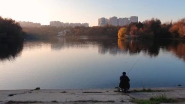 Balıkçı bir adamın gölde olta atıp dinlendiği günbatımı sahnesi. Durgun su yüzeyine yansıyan renkli ağaçlarla güzel bir sonbahar mevsimi..