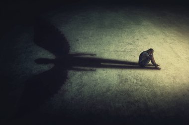 Karanlık bir odada yalnız başına oturan bunalımlı genç adam güçlü bir koruyucu meleğin gölgesini oluşturuyor. İç güç kavramsal arka plan. Stresli bir insan, hayali bir arkadaşıyla içe kapanık.