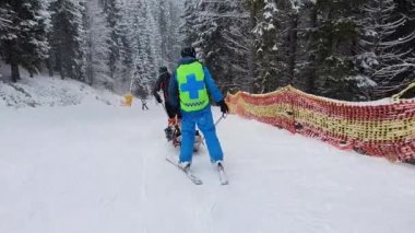 Dağ kurtarma ekipleri yaralı bir kayakçıyı taşıyorlar, ilk yardım sonrası yokuş aşağı gidiyorlar. Yokuş kurtarma, kayak devriyesi özel bir kızakla kurbanı tahliye ediyor. Bukovel kayak merkezi, Ukrayna Karpatları.