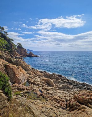 Deniz dalgalarının yavaşça kayalık kıyı şeridine çarptığı güneşli kıyı manzarası. Blanes (Costa Brava), İspanya 'da Cala sant Francesc Sahili' nin güzel turkuaz su kıyıları