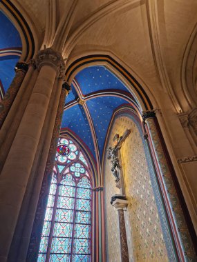 Paris, Fransa - 10 Aralık 2025: Notre-Dame 'daki bir şapelin iç görünümü. Duvarda asılı duran haç, altın yıldızlarla dağılmış parlak mavi tavanın altındaki vitraylı camla aydınlatılıyor.