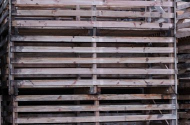 Büyük, yıpranmış ahşap sandıklar ya da kenarları kesilmiş teneke kutular. Paralel kereste kalasları karanlık, endüstriyel ya da tarımsal bir zemine karşı tekrarlı geometrik desen oluşturur..