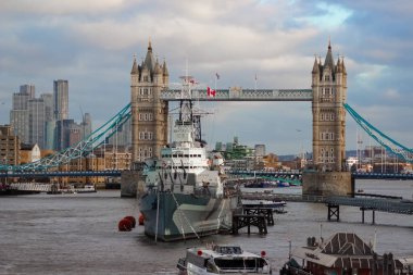 Londra, Birleşik Krallık - 25 Aralık 2025: Londra 'daki Thames Nehri manzaralı bir manzara, tarihi HMS Belfast kruvazörü, uzaktaki ikonik Tower Bridge ve şehrin bulutlu silueti boyunca uzanan Londra Kulesi.