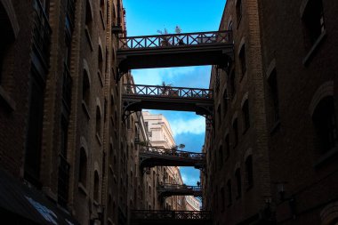 Londra, Birleşik Krallık - 25 Aralık 2025: Londra 'nın tarihi Shad Thames' inin dar bir görüntüsü, mavi gökyüzü altında ikonik demir geçitlerle birbirine bağlı Viktorya dönemi tuğla depolarını gösteriyor. Endüstriyel miras ve şehir hayatının mükemmel bir karışımı..