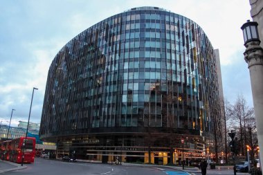 Londra, Birleşik Krallık - 25 Aralık 2025: Modern, cam kaplı Park Plaza Westminster Bridge Hotel. Kırmızı çift katlı bir otobüs eğimli binadan geçiyor ve Güney Şeria 'daki ana konumunu vurguluyor..