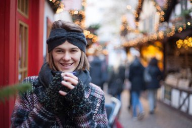 Almanya 'da geleneksel Noel pazarında dururken elinde bir bardak sıcak şarap tutan güzel bir kadın. Kışın giyilen neşeli modelin portresi Noel ruhunun tadını çıkarıyor..