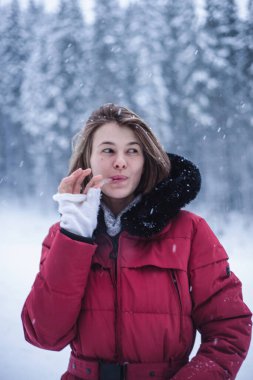 Kış kıyafetli güzel bir kadın kış karlarında dikilirken buz sarkıtını komik bir şekilde yalıyor. Etrafı karlarla çevrili ve kış tatilinde eğlenen mutlu kadın portresi..