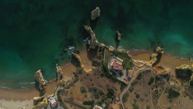 Portekiz 'in Lagos şehrinde Atlantik' in yonttuğu altın kayalıkların, deniz mağaralarının ve kaya oluşumlarının hava perspektifleri. Kemerler arasında küçük plajları olan popüler seyahat noktalarının insansız hava aracı görüntüsü, berrak, turkuaz suyu olan kayaların oluşumu.