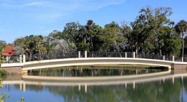 Güzel kemerli bir köprü, etrafındaki ağaçları ve açık gökyüzünü yansıtan sakin bir göl boyunca güneşli bir günde St. Augustine, Florida 'daki La Leche Tapınağı' ndaki arazide uzanır.