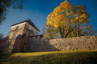 Ortaçağ şatosunun parlak güneşle aydınlanan bir bölümü. Fotoğraf kaba taş ve tuğladan yapılmış güçlü, yüksek bir duvar tarafından yönetiliyor. Yuvarlak bir gözetleme kulesi duvarın arkasından yükseliyor..
