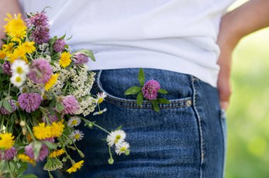 Mavi kot pantolon giyen, elinde kır çiçekleri, doğa konsepti, günlük yaşam tarzı, yaz tatili ve çiçeklerle gezen bir kadın.