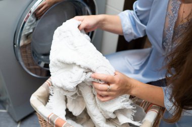 Çamaşır sepetinden kirli çamaşırları çıkaran ve çamaşır makinesine koymaya hazırlanan kadın. Ev işleri ve ev temizliği kavramı.