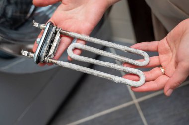 Çamaşır makinesinin ısıtıcısını elinde ağır kireçtaşı birikintisiyle tutan, ev aletlerinin onarımını, temizliğini ve bakımını gösteren kişinin yakın plan fotoğrafı.