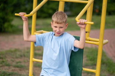 Odaklanmış genç çocuk dışarıda spor aletlerini kullanarak güç topluyor ve sıcak bir yaz gününde parkta formda kalıyor.