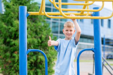 Parktaki maymun barlarının yanındaki neşeli sarışın çocuk gülümsüyor ve güneşli bir günde açık havada oynamaktan zevk alıyor.