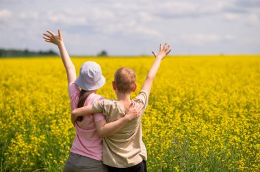 Elleri havada mutlu çocuklar. Çiçek açan sarı kolza tohumu tarlasında yazın tadını çıkarıyorlar.