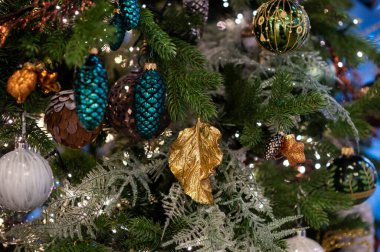 Altın ve gümüş Noel mücevherleri parıldayan ışıklarla süslenmiş ağaç dallarına asılarak klasik mevsimsel zarafetle parlak bir bayram atmosferi yaratıyor.