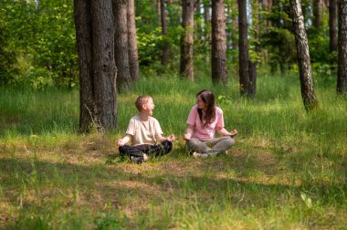 Anne ve oğlu nilüfer çiçekleri içinde meditasyon yapıyor ve gülüyor. Orman çayırlarında poz veriyor, birlikte doğanın ve zamanın tadını çıkarıyor.