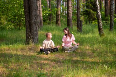 Anne ve oğlu nilüfer çiçekleri içinde meditasyon yapıyor ve gülüyor. Orman çayırlarında poz veriyor, birlikte doğanın ve zamanın tadını çıkarıyor.