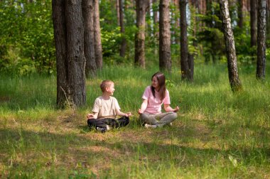 Anne ve oğlu nilüfer çiçekleri içinde meditasyon yapıyor ve gülüyor. Orman çayırlarında poz veriyor, birlikte doğanın ve zamanın tadını çıkarıyor.