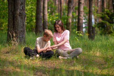 Anne ve oğlu bir ormanda yan yana oturmuş avuçlarındaki bir şeye bakıyorlar.