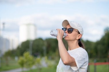 Açık hava spor sahasında idmandan sonra su içen genç bir kadın, sağlıklı yaşam tarzı, susuzluk ve aktif eğlence kavramı