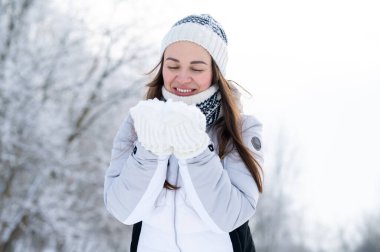 Kar parkında yürürken sıcak beyaz ceket ve eldiven giyen mutlu bir kadın. Sıcak kış yaşam tarzı, olumlu duygular, soğuk hava modası, açık hava eğlencesi ve refah konsepti.