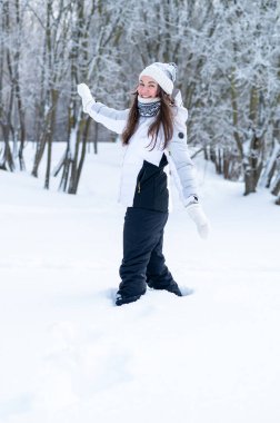 Sıcak kış giysileri içinde genç bir kadın karlı bir ormanda duruyor ve sessizliğin, temiz havanın ve huzurlu kış doğasının tadını çıkarıyor.
