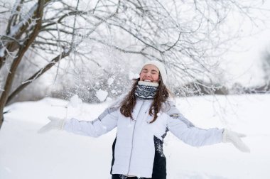 Neşeli kadın karlı bir kış parkında havaya kar fırlatıyor, neşeli mevsimlik bir an.