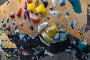 Profesyonel bir spor salonunda çeşitli parlak tırmanışları olan ahşap bir kaya duvarın yakınında. Aktif yaşam tarzı kavramı, ekstrem sporlar, fiziksel eğitim ve yetişkinler ve çocuklar için kapalı alan hobisi
