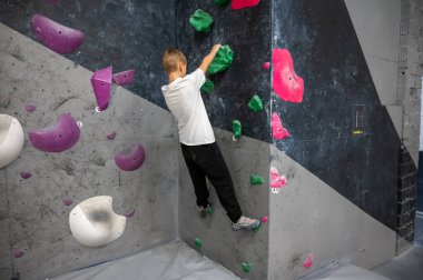 Beyaz tişörtlü ve siyah pantolonlu bir öğrenci karanlık bir duvarda antrenman yapıyor. Spor dersi sırasında ya da evde boş vakitlerinde profesyonel bir kaya atölyesinde tutunmaya çalışıyor.