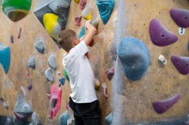 Koyu dokulu kaya duvarda parlak sarı bir tutuşa uzanan çocuk elinin detaylı bir görüntüsü. Öğrenci, tırmanma dersi sırasında ya da aktif hobisi sırasında profesyonel bir spor salonunda eğitim görüyor.