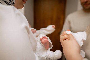 Beyaz vaftiz kıyafetleri içinde bebek taşıyan anne kolları ve kilisede küçük çoraplar tutan eller aile içi sevgi ve vaftiz töreninin dini geleneği.