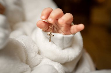 Çocukluk masumiyetinin korunması ve yumuşak ışıkta değerli bir hediye olan altın mücevher zincirini, haçlı kolyeli, kavramsal bir fotoğraf çeken bir bebeğin şefkatli anı.