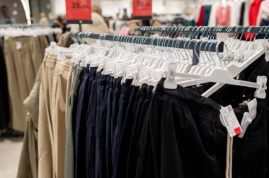 Perakende satışı için kırmızı etiketli parlak bir dükkanda koyu mavi ve bej renkli pamuklu pantolonlar içeren büyük bir modern kıyafet seçimi.