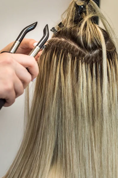 master makes hair extensions to a woman. Close-up of the process. Vertical photo