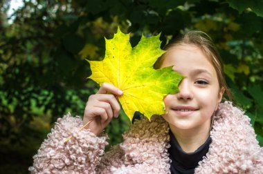 Yüzünde akçaağaç yaprağı olan neşeli bir kız. Sonbahar konsepti
