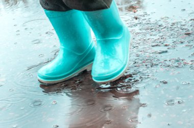 Yağmur sırasında su birikintisinde çocukların lastik mavi botları.