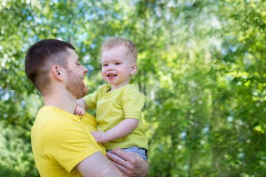 Oğlu babasının kollarında gülüyor. Yaz, park