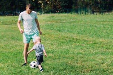 Oğlu ve babası yazın çimenlerde futbol oynuyorlar.