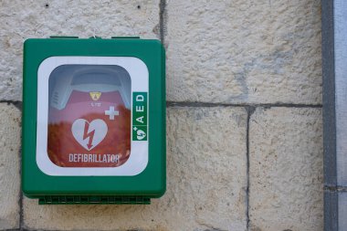 STOMORSKA, CROATIA, 08.27.2025: Parlak yeşil duvara monte edilmiş bir dolap, açıkça etiketlenmiş ve korunmuş kırmızı bir defibrilatöre ev sahipliği yapar. Kamu güvenliği ve ilk yardım hazırlığı için ideal olan bu birim, hızlı erişim, acil durum hazırlığı ve sağlık hizmetlerine önem vermektedir. 
