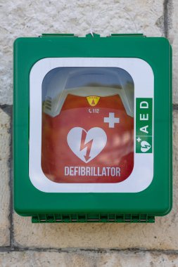 STOMORSKA, CROATIA, 08.27.2025: Parlak yeşil duvara monte edilmiş bir dolap, açıkça etiketlenmiş ve korunmuş kırmızı bir defibrilatöre ev sahipliği yapar. Kamu güvenliği ve ilk yardım hazırlığı için ideal olan bu birim, hızlı erişim, acil durum hazırlığı ve sağlık hizmetlerine önem vermektedir. 