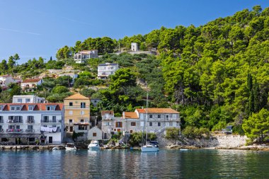 Beyaz ve pastel binalarla kaplı pitoresk bir liman, turkuaz sularda sallanan küçük tekneler ve sakin kıyı yaşamını, boş zamanlarını ve büyüleyici Akdeniz manzarasını yakalayan kayalık ön plan.