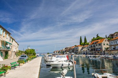 Beyaz ve pastel binalarla kaplı pitoresk bir liman, turkuaz sularda sallanan küçük tekneler ve sakin kıyı yaşamını, boş zamanlarını ve büyüleyici Akdeniz manzarasını yakalayan kayalık ön plan.