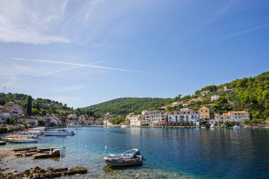 Beyaz ve pastel binalarla kaplı pitoresk bir liman, turkuaz sularda sallanan küçük tekneler ve sakin kıyı yaşamını, boş zamanlarını ve büyüleyici Akdeniz manzarasını yakalayan kayalık ön plan.